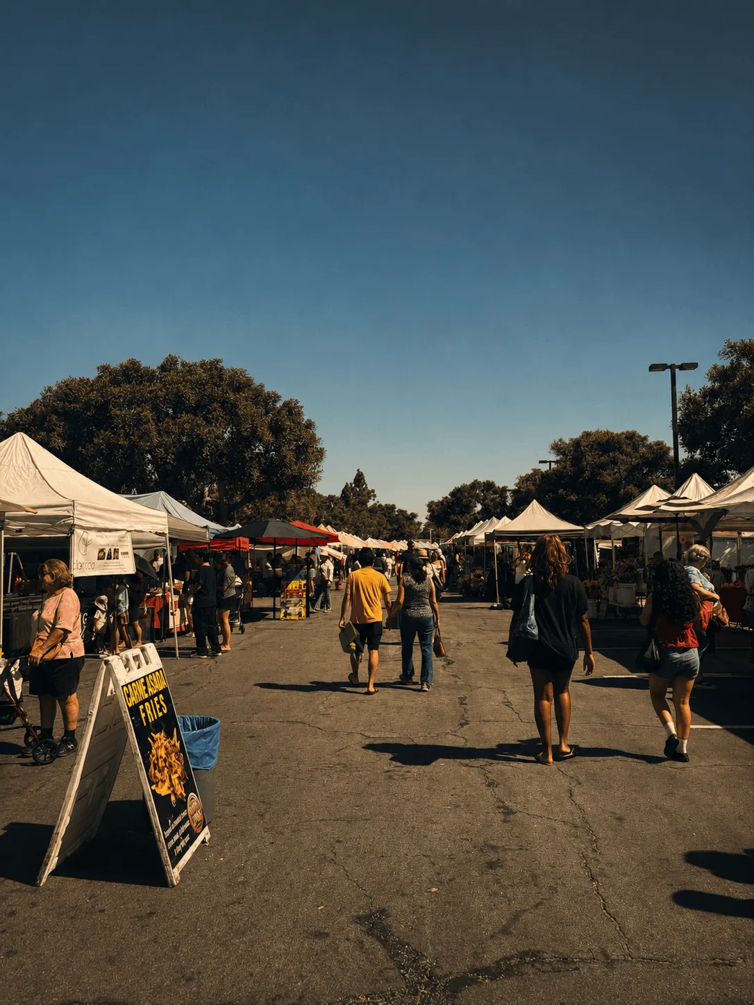 Clientes caminando por un pasillo ancho de carpas blancas de vendedores en un mercado de agricultores por la tarde en Cerritos, California